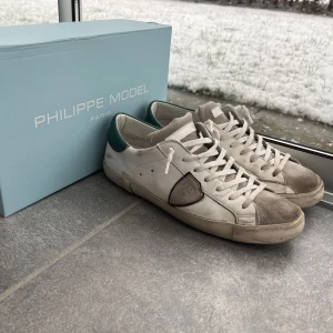 Vita sneakers från Philippe Model - Snygga vita sneakers från Philippe Model med grå detaljer och gröna hälpartier. Skorna har klassisk snörning och en stilren design som passar perfekt för en avslappnad look.
