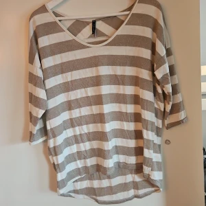 Randig tröja - Säljer en bekväm randig tröja i beige/glitter och vit. Tröjan har trekvartsärmar och en rund halsringning. Perfekt för en avslappnad stil. Hör av dig vid intresse!