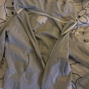 Grå hoodie med dragkedja - Säljer en grå hoodie med dragkedja och huva. Perfekt för en avslappnad stil. Den har praktiska fickor framtill och är tillverkad i ett mjukt material för extra komfort.