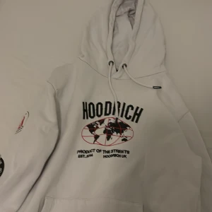 Vit hoodie från Hoodrich - Säljer en vit hoodie från Hoodrich med tryck på bröstet och ärmen. Hoodien har en justerbar huva med dragsko och en stor ficka framtill. Perfekt för en avslappnad stil.