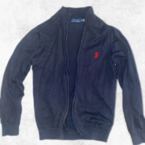 Mörkblå Ralph Lauren full zip - Säljer en stilren mörkblå full zip från Ralph Lauren. Den är i fint skick och har inga defekter eller liknande. Storleken är M och nypriset ligger på ca 2300 kronor. Den är perfekt för både vardag och mer uppklädda tillfällen.