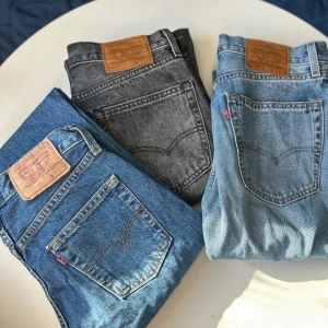 Levi's jeans i olika färger - Säljer tre par Levi's jeans i olika färger. Ett par i klassisk blå denim, ett par i ljusblå denim och ett par i grå denim. Perfekta för en avslappnad stil. Märkesetiketten syns tydligt på alla paren.