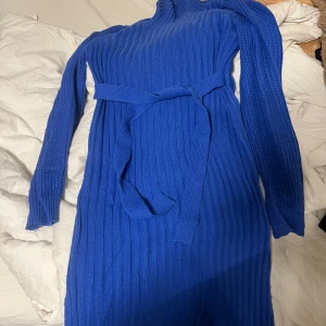 Blå ribbad klänning med bälte - Snygg blå ribbad klänning med långa ärmar och ett matchande bälte i midjan. Perfekt för en stilren look. Klänningen har en bekväm passform och är gjord i ett mjukt material.