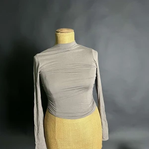 Grå långärmad polotopp - Säljer en stilren grå polotopp med långa ärmar. Toppen har en tight passform och är tillverkad i ett mjukt och stretchigt material. Perfekt för lager-på-lager eller som den är.