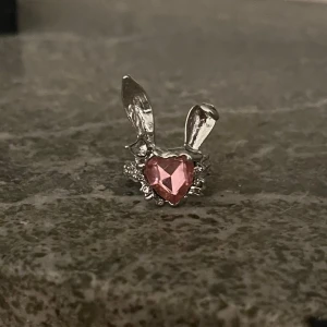 Silverring med kaninöron och rosa hjärta - Unik silverring med kaninöron och ett rosa hjärta i mitten. Ringen har en lekfull design med detaljerade öron och en glittrande rosa sten som ger en söt touch.