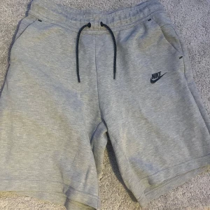 Grå snygga shorts från Nike  - Säljer ett par grå Nike shorts med elastisk midja och snörning. De har en diskret Nike-logga på vänster ben och praktiska fickor med dragkedja. Perfekta för en avslappnad stil. Dom är köpa på JD i England och dom har inte används så mycket.