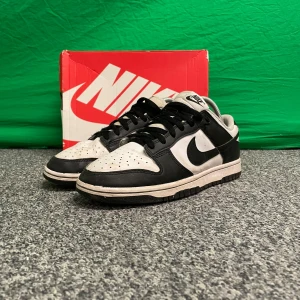 Panda Dunks - Snygga Nike Dunk sneakers i klassisk svart och vit färgkombination. Skorna har en stilren design med snörning och en bekväm passform. Perfekta för en sportig look.