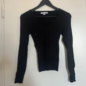 Svart ribbad tröja - Svart ribbad tröja med v-ringning. Tröjan har långa ärmar och en tight passform, använd med bra skick.