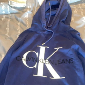 Blå hoodie från Calvin Klein Jeans - Säljer en snygg blå hoodie från Calvin Klein Jeans med stor vit CK-logga på framsidan. I storlek L