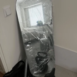 Rektangulär spegel med plastskydd - Säljer en stor rektangulär spegel som fortfarande har plastskyddet kvar. Perfekt för att ge rummet en modern touch.