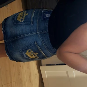 Jeanskjol från Victoria Beckham - Snygg jeanskjol från Victoria Beckham med coola guldbroderade kronor på bakfickorna. Kjolen har en klassisk blå jeansfärg och stolen L men passar mig som har S 
