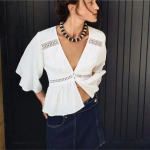 Vit blus med spetsdetaljer - Säljer en elegant vit blus med v-ringning och spetsdetaljer. Blusen har trekvartsärmar och knappar framtill. Perfekt för en stilren look. Sista bandet  är lite lös men inget man tänker på!💕