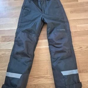 Grå täckbyxor från Cross Sportswear - Säljer ett par grå täckbyxor från Cross Sportswear. Byxorna har reflexdetaljer vid benen och justerbara benslut. Perfekta för kalla och blöta dagar.