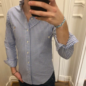 Blå och vit rutig skjorta från Ralph Lauren - Säljer en stilren blå och vit rutig skjorta från Ralph Lauren. Skjortan har en slim fit passform och är tillverkad i stretchigt oxfordmaterial. Den har långa ärmar och knappar framtill samt en broderad logotyp på bröstet. Modellen är ca 182, tveka inte att kontakta vid eventuella frågor 😀
