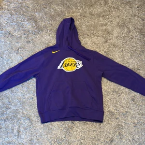 Lila Los Angeles Lakers hoodie från Nike - Säljer en snygg lila hoodie från Nike med Los Angeles Lakers-logga på bröstet. Hoodien har en klassisk känguruficka och en justerbar huva. Perfekt för alla Lakers-fans! 🏀