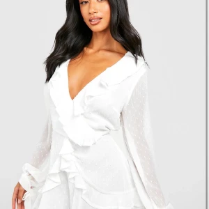 Vit klänning/playsuit från Boohoo - Säljer en elegant vit klänning från Boohoo med volangdetaljer. Klänningen har långa ärmar och en v-ringad design som ger en stilren look. Perfekt för sommaren eller student. Aldrig andvänd. Skulle att den har storlek S/M☺️