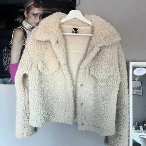Beige teddyjacka - Mysig beige teddyjacka i mycket bra skick. Perfekt för höst och vinter med sin fluffiga och varma design. Jackan har långa ärmar och knappar framtill. 