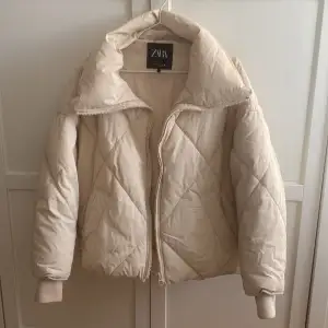 Säljer en superfin beige oversized pufferjacka från ZARA i storlek XS. Använd väldigt fåtal gånger så i fint skick! Jackan är quiltad och har en dragkedja framtill. Den är perfekt för höst och vinter. Jackan har långa ärmar och en justerbar dragsko i nederkanten för bästa passform.