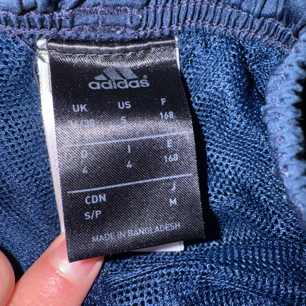 Säljer ett par mörkblå träningsbyxor från Adidas i bra skick. De har de klassiska vita ränderna längs sidorna och en elastisk midja för extra komfort. Perfekta för träning eller en avslappnad dag. 🏃♀️. Farkut & Housut.
