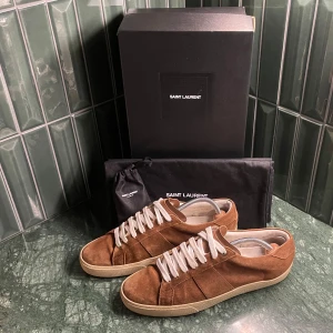 Saint Laurent skor - Säljer ett par snygga bruna sneakers i mocka från Saint Laurent. De har en klassisk design med vita snören och en bekväm sula. Skorna är i mycket bra skick och kommer med originalförpackning. Storlek 42 men passar även 43. 