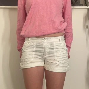 Vita cargo shorts med knappar - Säljer ett par vita cargo shorts i bomull med knappar framtill och bakfickor med knappdetaljer. De är perfekta för sommaren och har en avslappnad passform. 