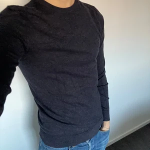Mörkblå stickad tröja  - Säljer en stilren mörkblå tröja från Lindeberg. Den är långärmad och har en diskret broderad logga på bröstet. Perfekt för både vardag och lite finare tillfällen. Tröjan är i bra skick är i storlek S. Hör gärna av er vid funderingar eller frågor!