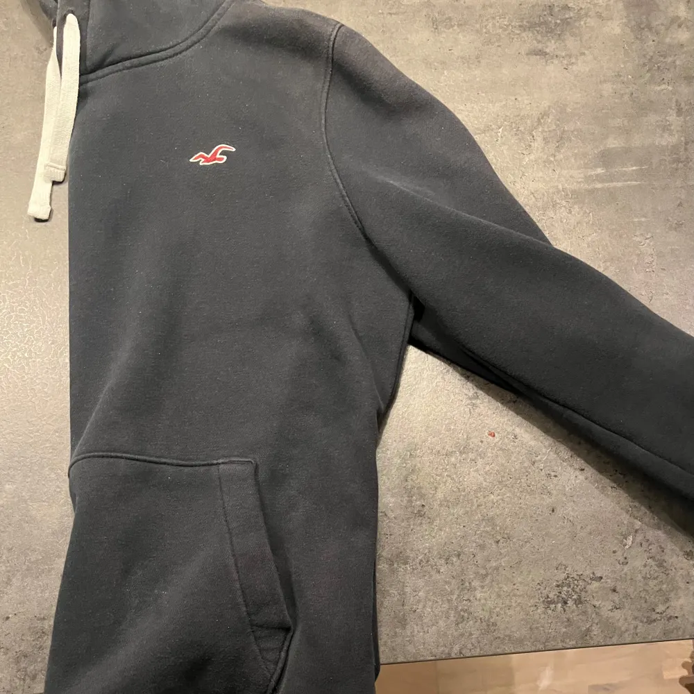 Säljer en snygg och bekväm mörkblå hoodie från Hollister. Den har en klassisk design med en liten logga på bröstet och justerbara snören i huvan. Perfekt för en avslappnad stil och passar till de flesta tillfällen. Den är i bra skick och redo för en ny ägare!. Tröjor & Koftor.