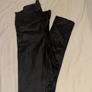Svarta byxor från Vera moda - Snygga svarta byxor från Vera moda i ett glansigt material. Perfekta för en kväll ute eller en fest. De har en klassisk design med fickor och dragkedja. Passar bra till både vardag och festligare tillfällen.