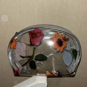 Blommig transparent necessär - Säljer en superfin transparent necessär med blommönster. Den har en dragkedja upptill och är perfekt för att hålla ordning på smink eller småprylar. Blommorna i rosa och orange ger en härlig sommarkänsla. Perfekt för resor eller som en söt detalj i badrummet!
