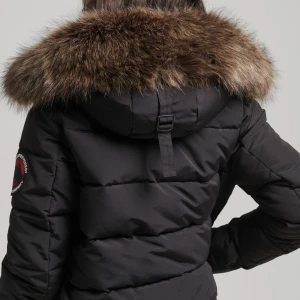 Svart Superdry Everest jacka - Svart Superdry vinterjacka med blå och svart logga. Elastisk midja, avtagbar huva, avtagbar päls på huvan. Foder 100% nylon. Mycket varm och hållbar. Jackan har normal passform och långa ärmar. Flera fickor, dragkedja och knappar framtill. Jackan är använd ett par gånger så den har några skrynklor och lite ludd men i övrigt i mycket bra skick. Storlek 40 låter större, men sitter bra och passar även bra till hoodie och jacka.🧥💕