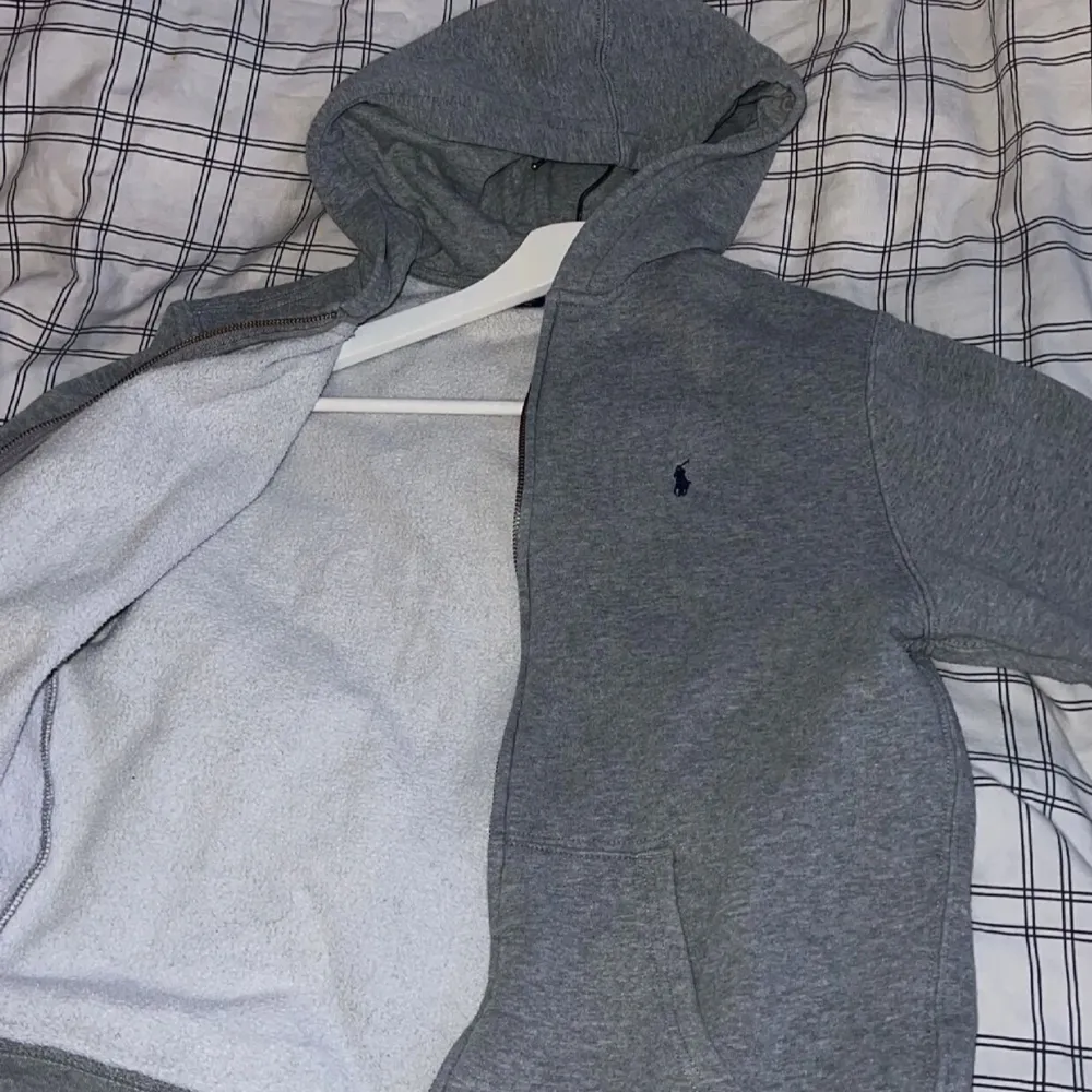 Säljer en snygg och bekväm grå hoodie från Polo Ralph Lauren. Den har en dragkedja framtill och en klassisk logga på bröstet. Perfekt för kyliga dagar eller som ett stilrent lager under jackan. Passar både till vardags och avslappnade tillfällen.. Tröjor & Koftor.