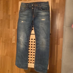 Blå jeans med slitningar - Säljer ett par snygga blå jeans med coola slitningar på framsidan. De har en klassisk femficksdesign och en knappgylf. Perfekta för en avslappnad stil och passar till de flesta tillfällen. Skicket är bra med en skön, inburen känsla.