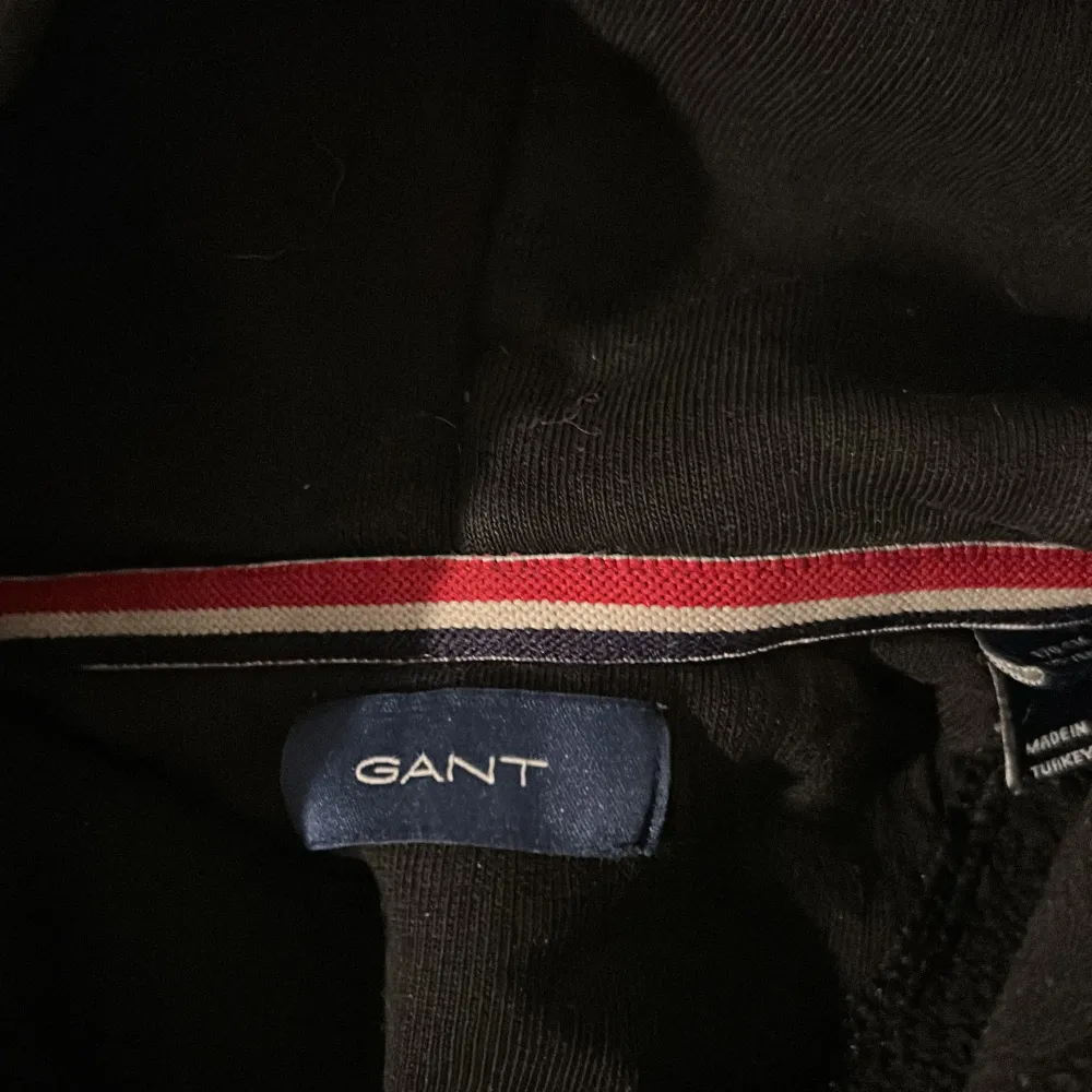 Säljer en snygg svart hoodie från GANT med deras klassiska logga och ett coolt emblem på bröstet. Perfekt för höst och vinter, den är både stilren och bekväm. Passar lika bra till skolan som till en chill dag hemma. Hör av dig om du är intresserad!. Neuletakit & Villapaidat.