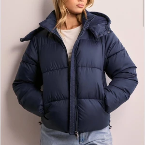 Mörkblå pufferjacka - Säljer en snygg mörkblå pufferjacka som är perfekt för kyliga dagar. Jackan har en dragkedja framtill och en mysig huva. Den är i normal passform och passar perfekt till vintern nu. Superbekväm och stilren! Helt slutsåld på hemsidan, endast använd en månad ungefär