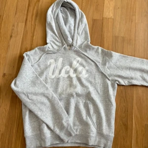 Grå hoodie från UCLA - Säljer en grå hoodie från UCLA i bra skick. Den är supermjuk och perfekt för kyliga dagar. Hoodien har en stor ficka fram och en bekväm huva. Perfekt för både vardag och mysiga hemmakvällar!