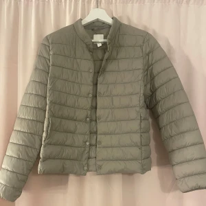 Beige pufferjacka från H&M - Säljer en snygg beige pufferjacka från H&M i storlek 38. Jackan har en stilren design med knappar framtill och långa ärmar. Skriv för mer detaljer 💕