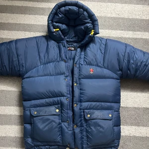 Blå dunjacka  - Säljer en blå dunjacka från Fjällräven Polar i mycket bra skick. Den är perfekt för kalla vinterdagar och har en justerbar huva. Perfekt för dig som vill hålla dig varm i vinter! ❄️Den är extra stor!! Känn dig fri att pruta priset!😁