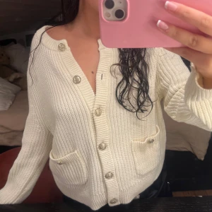 Vit stickad kofta med knappar - Säljer en superfin vit stickad kofta med snygga knappar framtill. Den har två praktiska fickor och en skön passform. Perfekt för både höst och vår när du vill ha något mysigt men stilrent. Passar till alla tillfällen! 💫färgen är mellan vit och krämfärgad