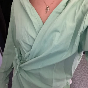 Mintgrön omlottskjorta - Säljer en superfin mintgrön omlottskjorta med knytning i midjan. Skjortan har långa ärmar med knappar vid ärmsluten. Perfekt för vår och sommar! 💚