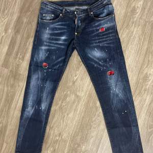 Säljer ett par coola jeans från Dsquared2 i mörkblå denim med slitna detaljer och röda lappar. De har en slim passform och är perfekta för en avslappnad stil. Märkeslappen på baksidan ger en extra touch av stil. Perfekta för höst och vår! Storlek 40. Priset kan diskuteras!