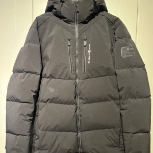 Svart dunjacka från Sail Racing - Säljer en svart dunjacka från Sail Racing i mycket bra skick. Jackan är i storlek XL men passar L. Perfekt för vintern med sin höga fyllkraft på 500. Den har en dragkedja framtill och två bröstfickor med dragkedjor.  Nypris 4000:-