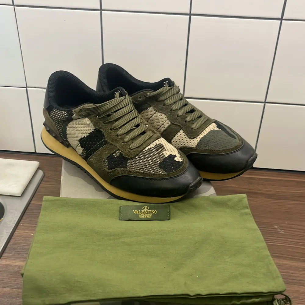 Säljer ett par snygga Valentino Rockrunner sneakers i camouflage. De har en cool mix av gröna och svarta nyanser med mocka och syntetmaterial. Skorna har snörning och en bekväm sula, perfekt för en stilren look. De kommer med originalkartong och dustbag.. Skor.