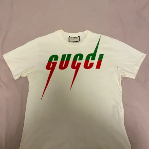 Gucci T-shirt Loose fit - Säljer en snygg vit t-shirt från Gucci med deras ikoniska logga i rött och grönt på framsidan. Perfekt för en casual look eller att styla upp med en kavaj. T-shirten är i bra skick och gjord av mjuk bomull. Passar perfekt till både vardag och fest!