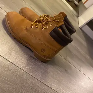 Säljer ett par klassiska bruna Timberland boots i skinn. De har snörning och är perfekta för höst och vinter. Skorna är i bra skick och har en robust design som passar både stad och natur. Perfekta för dig som vill ha stil och funktion i ett!