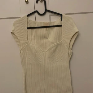 Beige ribbad topp - Säljer en snygg beige ribbad topp med korta ärmar. Den har en v-ringad design som ger en stilren look. Perfekt för både vardag och festliga tillfällen. Passar bra till jeans eller kjol!
