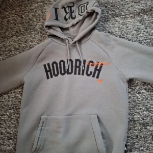 Grå hoodie och byxa från Hoodrich storlek XS - Säljer en snygg grå hoodie och byxa  storlek XS från Hoodrich med svart och orange text på bröstet. Den har en stor ficka fram och justerbar huva med snören. Perfekt för en casual look eller träning. Textdetaljer på ryggen ger en extra touch. Passar perfekt till höst och vår!