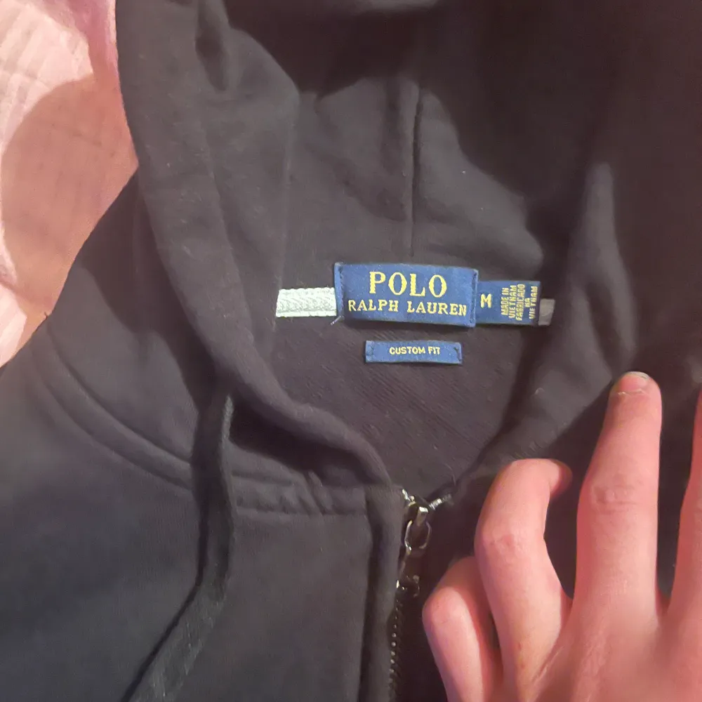 Säljer en snygg svart hoodie från Ralph Lauren i storlek M. Den har en dragkedja framtill och den klassiska loggan broderad på bröstet. Perfekt för både höst och vår, och passar till alla tillfällen. Superbekväm och stilren!. Tröjor & Koftor.