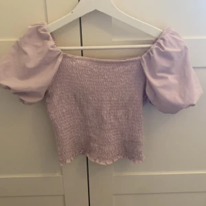 Ljuslila  topp från Gina Tricot - Säljer en superfin ljuslila offshoulder topp från Gina Tricot i storlek S. Toppen har puffiga korta ärmar och en smockad kropp som ger en snygg passform.💜 jättebra skick!
