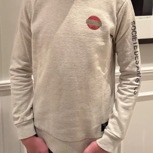 Beige tröja från Scotch & Soda - Säljer en snygg beige tröja från Scotch & Soda. Den har ett coolt tryck på ryggen och texten 'SOCIÉTÉ DES ARTISTES' på armen. Tröjan är i bra skick och passar perfekt till jeans. Hör av dig vid intresse samt frågor, pris är ej hugget i sten!🤩🤩