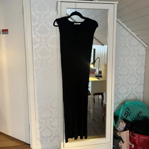 Svart ribbad klänning från NA-KD - Säljer en elegant svart ribbad klänning från NA-KD i storlek XS. Klänningen är ärmlös med en v-ringad design och har en lång passform. Perfekt för både vardag och festliga tillfällen. Den är i mycket bra skick och redo för en ny ägare!